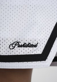 Tissu sportif en maille blanche avec de petits trous, mot brodé en noir « Interdit » et épaisse bordure noire le long du bord.