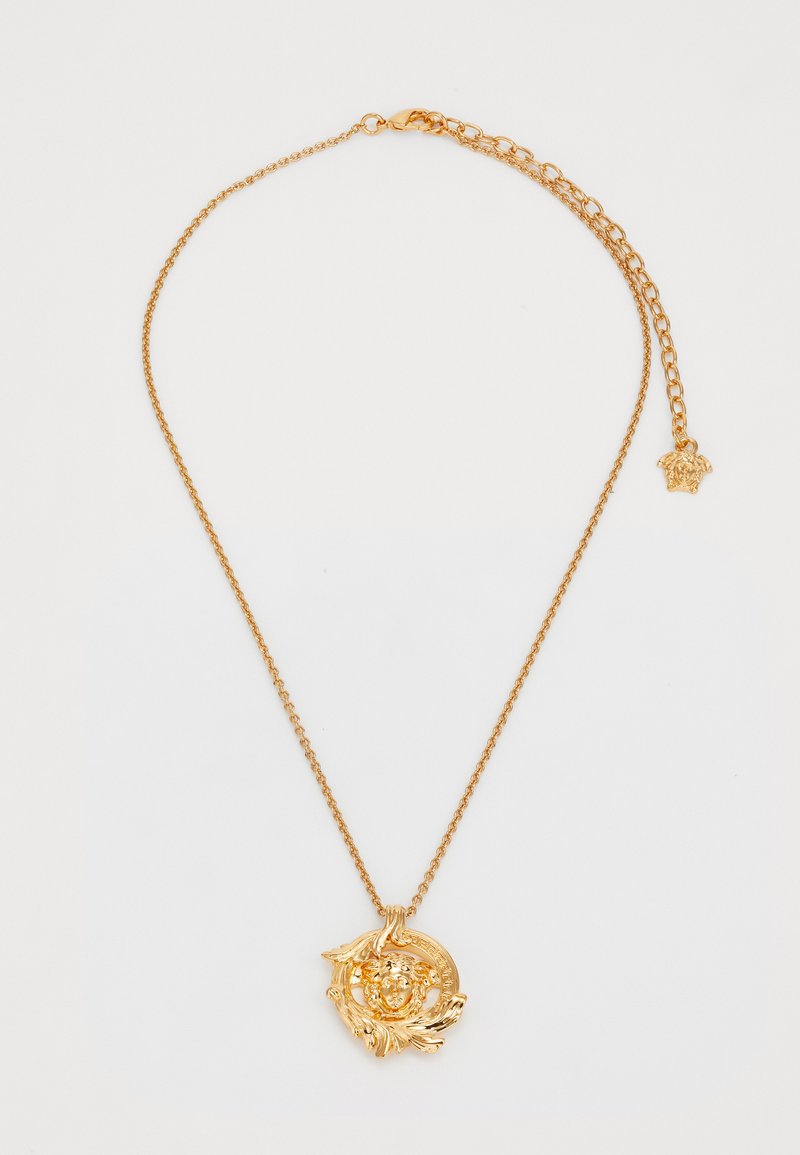 Collier en chaîne dorée avec un pendentif détaillé en forme de tête de Méduse et un petit charme Méduse sur le fermoir ajustable, sur fond blanc.