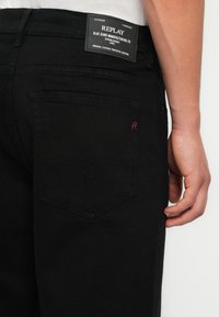Jeans negri din denim cu o croială standard, dotate cu o etichetă din piele pe talie și detalii subtile de cusătură roșie pe buzunarul din spate.