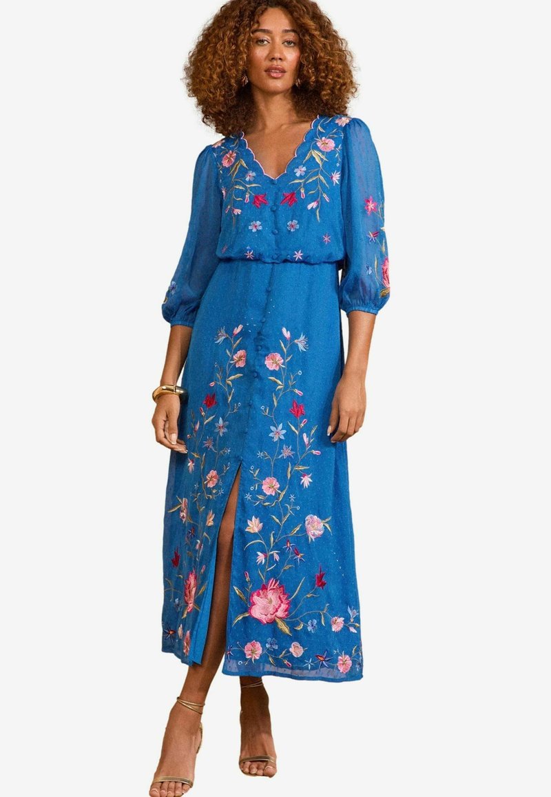 Blå broderad maxiklänning med blommönster, V-ringning och puffärmar. Har en sidoklyfta och dekorativa knappar framtill.