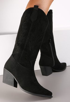 Bottes noires en daim montantes avec un orteil pointu, des découpes décoratives et un talon carré, dotées d'une fermeture à glissière latérale pour un enfilage facile.
