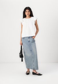 Hvit topp med volangermet, teksturert bodice, sammen med høyt liv, lyseblå denim skjørt og sorte flate sko med sirkulære detaljer.