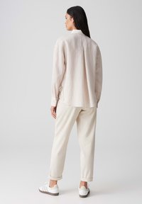 Lange mouwen, lichtbeige shirt met een textuurstof, zijstrikjes en een kraag, gecombineerd met crèmekleurige broeken en witte sneakers.