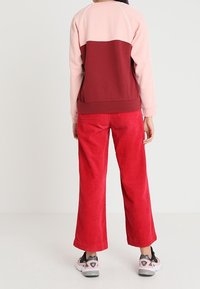 Rote Corduroy-Hosen mit weitem Bein, kombiniert mit einem farblich abgestimmten Sweatshirt in Rosa, Burgunder und Hellrosa. Mit kontrastierenden Nähten und sportlichen Sneakers.