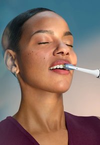 Frau mit geschlossenen Augen, die gegen einen sanften blauen Hintergrund die Zähne mit einer elektrischen Zahnbürste putzt.