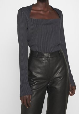 Donkere persoon met een geribd donkergrijs topje met een vierkante halslijn en zwarte leren broek met hoge taille.