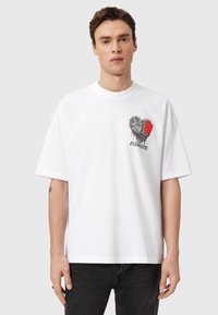 Λευκό βαμβακερό t-shirt με κοντά μανίκια που διαθέτει γραφικό σχέδιο καρδιάς σε μαύρο και κόκκινο. Χαλαρή εφαρμογή με στρογγυλή λαιμόκοψη.