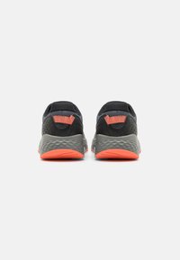 Zapatillas deportivas en negro y gris con parte superior de malla texturizada, cuello acolchado y suela de goma naranja. Tiradores dobles para ponerlas y quitarlas fácilmente.