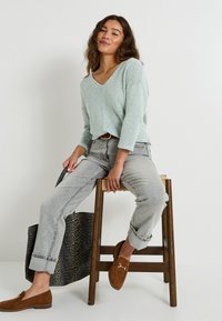 Suéter de punto de color azul claro con escote en V y mangas tres cuartos, combinado con jeans grises claros con puños y mocasines marrones. Bolsa de mano de estampado de leopardo.