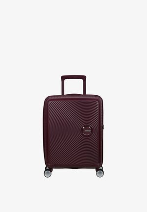 Valise rigide de couleur bordeaux avec un motif circulaire texturé. Équipée d'une poignée rétractable et de quatre roues multidirectionnelles.