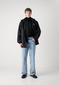 Black lightweight jacket with front buttons, black turtleneck, light blue wide-leg jeans, and black ankle boots with textured soles.