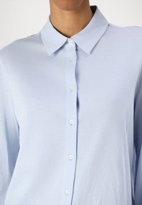 Light blue, long-sleeve shirt with a collar and button front. Soft texture with a smooth finish and pearlescent buttons.