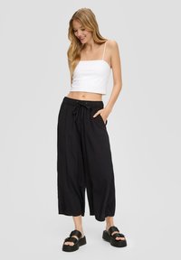 Zwarte cropped broek met een verstelbare tailleband, gecombineerd met een aansluitend wit hemdje. De gestylede look wordt aangevuld met platform sandalen.