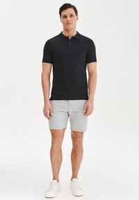 Czarny polo z krótkim rękawem i kołnierzykiem, w połączeniu z szarymi szortami. Model nosi białe trampki. Prosty, minimalistyczny design.