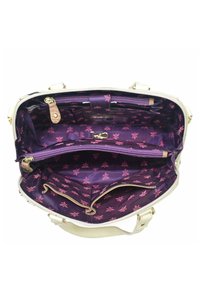 Weißer Handtasche mit lila floralem Innenraum, ausgestattet mit mehreren Fächern, Reißverschlüssen und goldfarbenen Beschlägen. Weiches Material mit strukturierter Form.