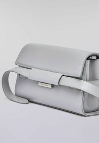 Borsa in pelle grigia con forma strutturata, chiusura a pattina e accento in metallo argentato con logo. Dotata di tracolla rimovibile.