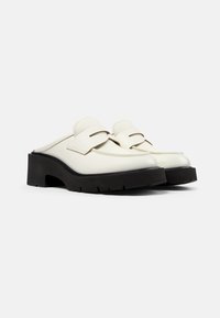 Witte leren instaploafers met dikke zwarte chunky platformzolen op een eenvoudige lichte achtergrond.