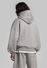 Felpa grigia con una vestibilità comoda, texture morbida e cappuccio. Presenta spalle scese e orlo a coste, abbinata a pantaloni corti coordinati.