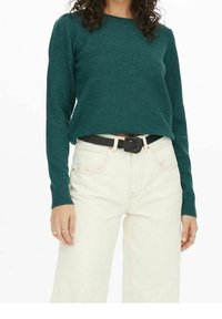 Maglione a maglia turchese con colletto tondo e maniche lunghe, abbinato a jeans crema a vita alta e una cintura nera, caratterizzato da un design semplice.