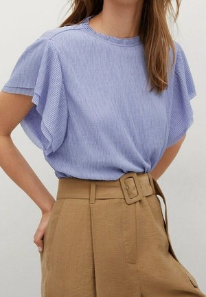 Top morado claro de manga corta con ribetes acanalados y mangas con volantes, combinado con pantalones de tiro alto color beige con un cinturón ancho y pliegues delanteros.