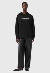 Felpa nera con logo bianco "ALLSAINTS LONDON", con tasca frontale e vestibilità comoda, abbinata a pantaloni in pelle nera a gamba larga e ballerine.