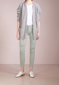 Harmaa neulottu villatakki pitkillä hihoilla ja kahdella etutaskulla, yhdistettynä vaaleanvihreisiin revittyihin farkkuihin ja valkoisiin nauhaliivikengiin.