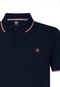 Námořnická modrá polo košile s límcem, který má červené a bílé pruhy, tři knoflíky a malé červené logo na levé hrudi.