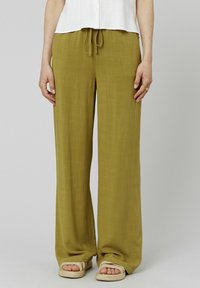 Un pantalon large de couleur vert olive, fabriqué en tissu léger avec une taille à cordon de serrage, associé à des sandales à semelle en corde.