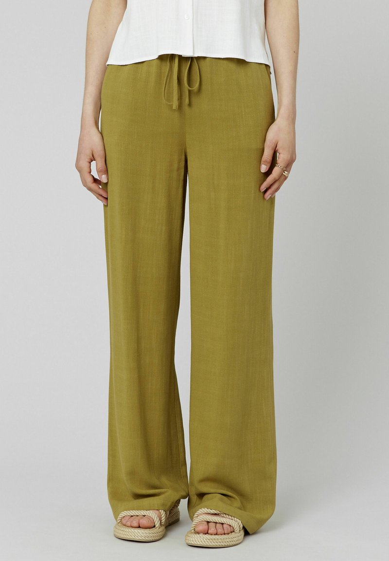 Un pantalon large de couleur vert olive, fabriqué en tissu léger avec une taille à cordon de serrage, associé à des sandales à semelle en corde.