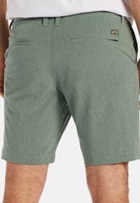 Shorts verts en tissu texturé et chiné. Dotés de deux poches arrière, de coutures minimales et d'une petite étiquette de marque cousue sur le côté droit.