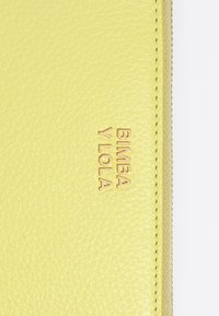 Cartera de cuero amarilla con superficie texturizada, que presenta el texto en relieve dorado "Bimba y Lola" y un cierre de cremallera a lo largo del borde.