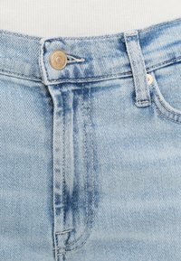 Svetlomodré rifľové nohavice majú stredne vysoký pás, zapínanie na jeden gombík a jemné vyblednuté vzory po celom materiáli.