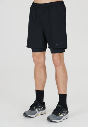 Svarta shorts med elastiskt midjeband, med en lätt design och innerväv, kombinerade med grå löparskor och svarta strumpor.