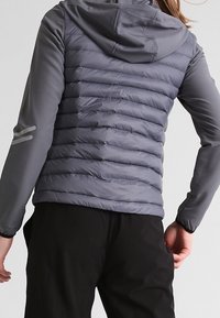 Harmaa toppatakki, jossa on huppu, tikatut osat, sileä kangas ja heijastavat yksityiskohdat hihoissa. Kevyt muotoilu.