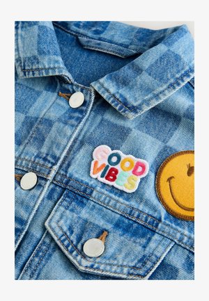 Džinsinė striukė su šviesiai mėlynu languotu raštu. Papuošta siuvinėtu "GERŲ EMOCIJŲ" pleistru ir geltonu šypsenėle pleistru. Sidabriniai mygtukai.