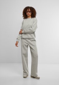 Pilkas džemperis ir plačių kojų kelnių komplektas, pagamintas iš minkštos medvilnės mišinio, pasižymintis laisvu siluetu, raukšlėtomis rankovėmis ir subtiliais siuvimo akcentais.