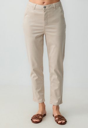 Pantalons beiges coupés avec une texture lisse, dotés d'une fermeture à boutonnage et à zip à l'avant, de poches latérales, et associés à des sandales marron.
