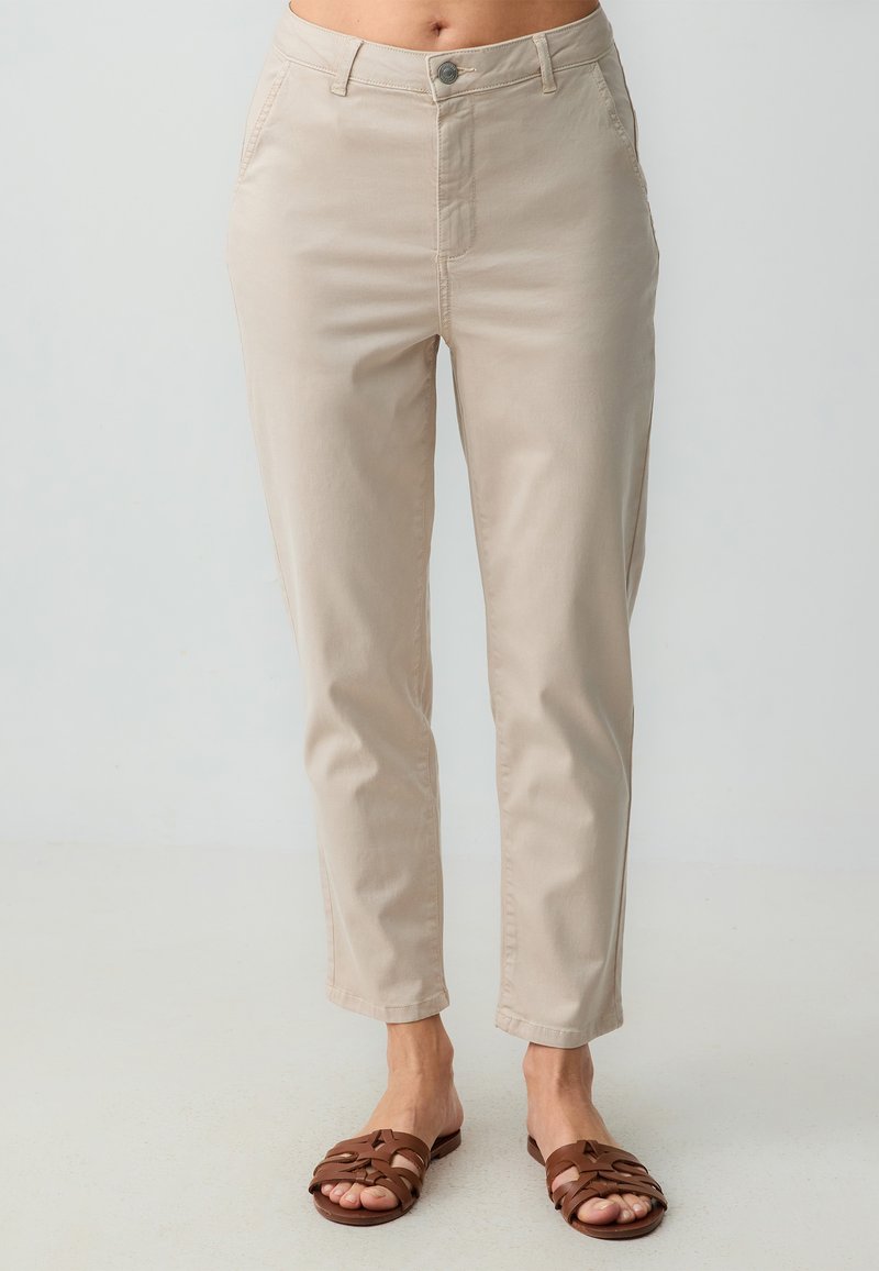 Beige cropped broek met een gladde textuur, voorzien van een haak- en ritssluiting aan de voorkant, zijzakken en gecombineerd met een paar bruine sandalen.