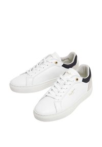 Witte leren sneakers met platte zolen, vetersluiting en donkere accenten; voorzien van gouden logo en stikdetails.