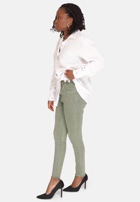 Hvid skjorte med knaplukning og struktureret stof, lysegrønne slim fit jeans og sorte højhælede sko. Synlig manchetdetalje og sidevisning.