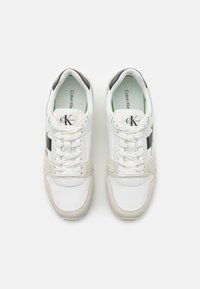 Sneaker bianche e grigie in materiale di pelle e rete, con design a lacci, logo prominente e suola in gomma testurizzata.