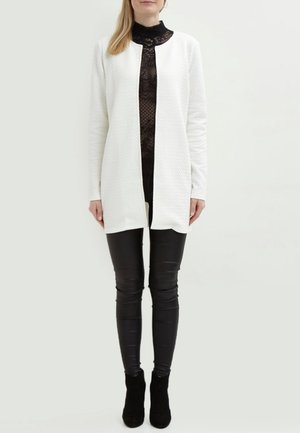White quilted long jacket with a round neckline, worn over a black lace top; paired with black leather pants and ankle boots.
