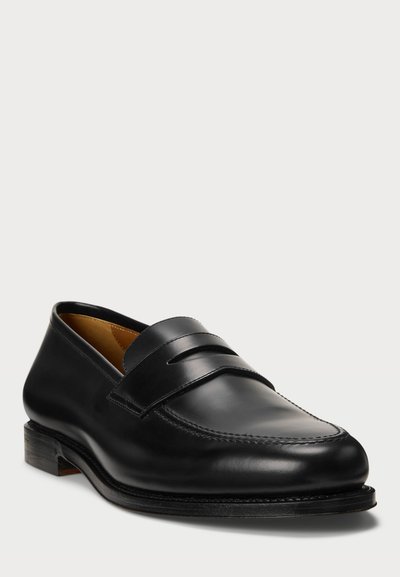 Mocasin de cuero negro con tacón plano, con dos acentos de cinta horizontal y una costura a lo largo del dedo del pie. Textura suave, diseño clásico.