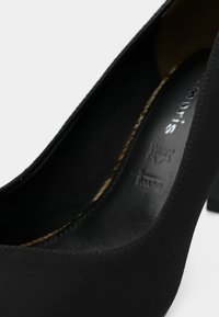 Μαύρο ψηλοτάκουνο παπούτσι με λείο, ματ φινίρισμα, στρογγυλή μύτη και χοντρό τακούνι. Το εσωτερικό διαθέτει σχέδιο στην επένδυση και λεπτομέρεια της μάρκας.