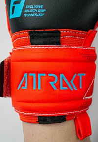 Gant de gardien de but rouge avec des paumes noires texturées, inscription bleue "ATTRAKT" et une sangle Velcro sécurisée pour le soutien du poignet.