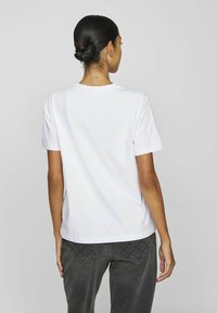 Hvit bomull T-skjorte med rund hals og korte ermer. Brukt sammen med grå jeans med quiltede baklommer. Enkelt design, ingen grafikk.