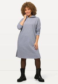 Vestido gris claro de manga larga con cremallera frontal y aberturas laterales. Llevado con botas de acordeón negras hasta la rodilla. Tejido suave y texturizado.