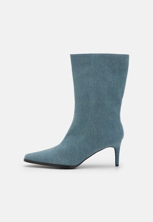 Bottine en denim bleu mi-hauteur avec bout pointu et talon aiguille fin, présentée sur fond blanc.