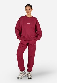 Burgundské mikina a odpovídající kalhoty vyrobené z měkké bavlny. Mikina má malé logo, uvolněný střih a ribbené manžety.