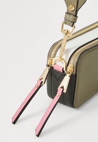 Sac rectangulaire en matériau synthétique olive et noir. Équipé de ferrures dorées, d'une double fermeture éclair et de sangles accentuées roses avec clips.